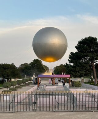 Image One: The Olympic Cauldron, an enormous golden orb, standing tall amidst lush greenery in Jardin des Tuileries in Paris, France.