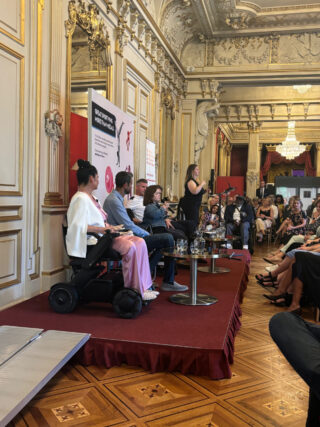 The four panellists mentioned sit on the stage, there is ramped access provided to the left hand side, and a BSL (British Sign Language) interpreter is positioned to the right. Sin&eacute;ad Burke speaks to the room.